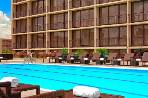 A clear blue pool with lounge chairs and towels, set against a modern building with large windows.