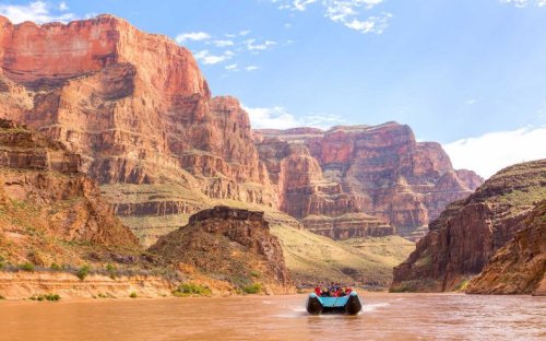 A group rafting on a river surrounded by towering red rock cliffs under a blue sky.