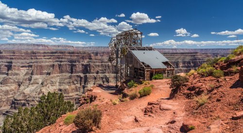 A viewing platform at the Grand Canyon, surrounded by rocky terrain and dramatic cliffs under a blue sky with clouds.