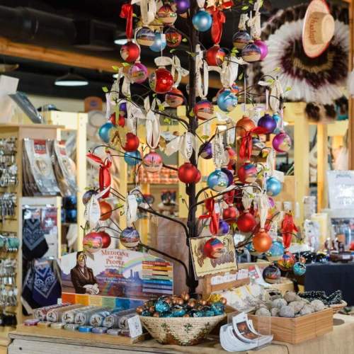 A decorative tree adorned with colorful ornaments and ribbons, surrounded by various crafts and gifts in a shop.