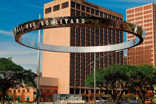 A large metallic ring sign reading "Post Oak Boulevard" above a modern building complex in an urban setting.