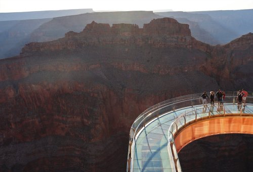 A glass bridge extends over a canyon, with visitors enjoying the stunning view of the rocky landscape below.