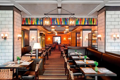 Modern restaurant interior with wooden accents, colorful artwork, and cozy seating arrangements. Warm lighting enhances ambiance.
