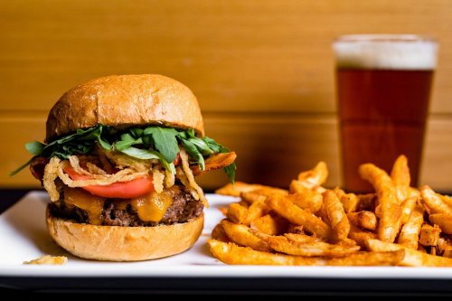 A juicy burger with cheese, lettuce, tomato, and crispy onions, served with curly fries and a glass of beer.