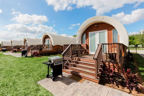A row of cozy, cabin-like structures with curved roofs, surrounded by green grass and a clear blue sky.