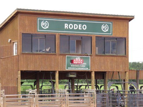 A wooden rodeo building with large windows and a sign displaying "WR RODEO" above.