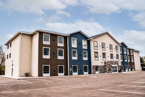 A modern, multi-story hotel building with a mix of beige and dark blue exterior, set against a cloudy sky.