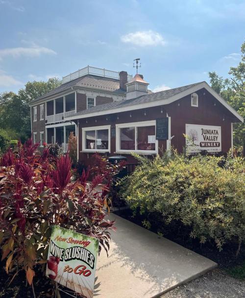 A charming winery building surrounded by colorful plants and a sign advertising wine slushies to go.
