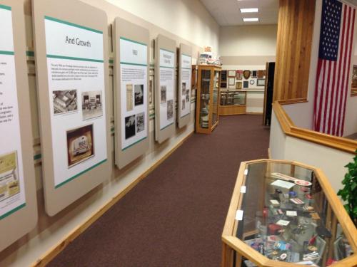 A museum hallway with informational panels on the walls and display cases showcasing various artifacts. An American flag is visible.