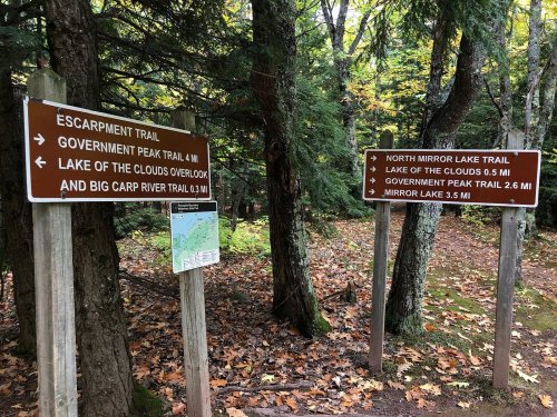 Trail signs in a forest, indicating directions and distances for various hiking trails.
