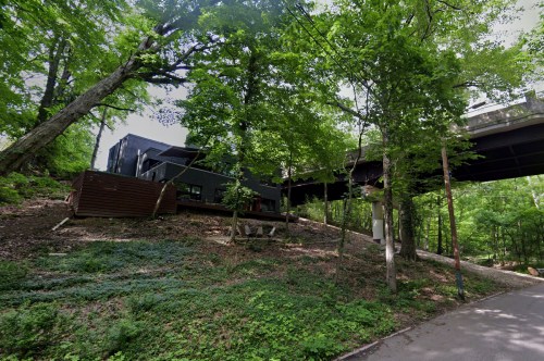A modern building nestled among lush green trees, with a pathway leading through the forest.