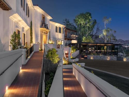 A beautifully lit pathway leads to a modern building, surrounded by lush greenery and a scenic hillside at dusk.