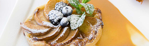 A dessert featuring a caramelized apple tart topped with berries and mint, drizzled with sauce.