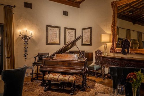 A vintage piano in a cozy room, surrounded by elegant decor, including framed music sheets and ornate mirrors.