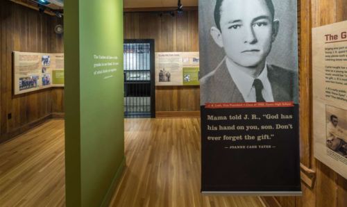 Interior of a museum exhibit featuring a banner with a black-and-white photo of a man and text about his life.
