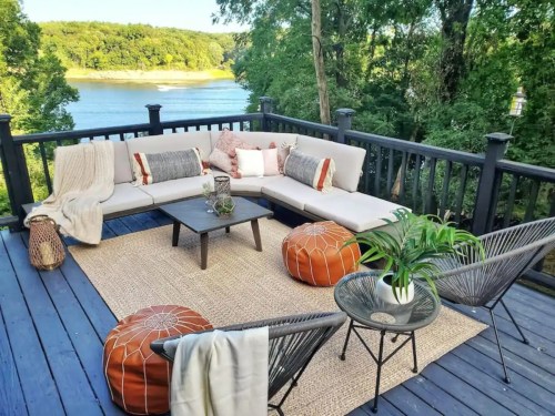 Cozy outdoor seating area with a sectional sofa, poufs, and a view of a river surrounded by trees.