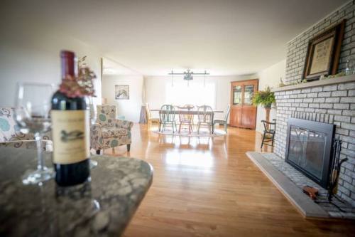 A cozy living room with a bottle of wine and glasses on a table, featuring a fireplace and dining area in the background.