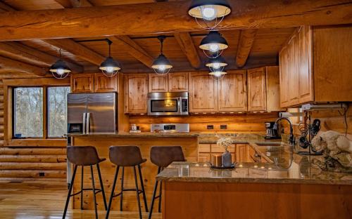 Cozy log cabin kitchen with wooden cabinets, modern appliances, and bar stools at a counter under pendant lights.