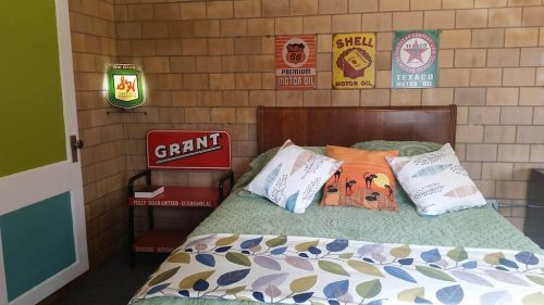 Cozy bedroom with a green bedspread, vintage oil signs on the wall, and a bedside table displaying a "Grant" sign.