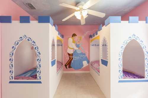 A whimsical children's bedroom with castle-themed beds and a mural of a prince and princess on a pink wall.