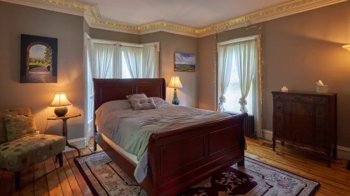 Cozy bedroom with a wooden bed, soft lighting, and elegant decor, featuring large windows and a patterned rug.