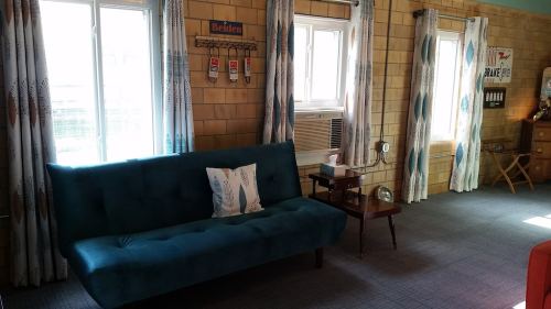 A cozy room featuring a teal sofa, wooden furniture, and large windows with patterned curtains.