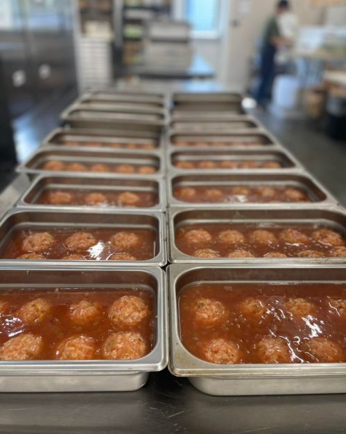Trays of meatballs in sauce lined up on a kitchen counter, ready for serving or storage.