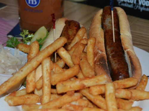 Two hot dogs in buns with toothpicks, served with a side of golden fries and a small dish of sauerkraut.
