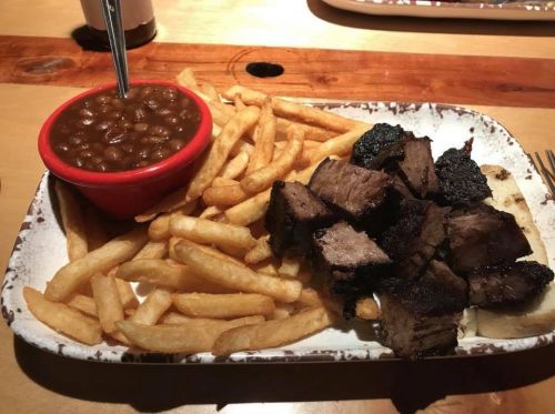 A plate with grilled meat chunks, crispy fries, and a bowl of baked beans on a rustic wooden table.