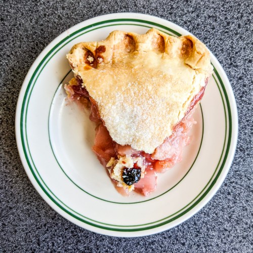 A slice of apple pie on a white plate with a green rim, resting on a gray countertop.