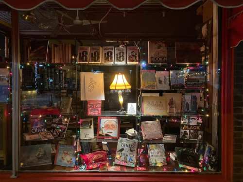 A cozy bookstore window display with colorful lights, books, and a lamp, creating a warm, inviting atmosphere.
