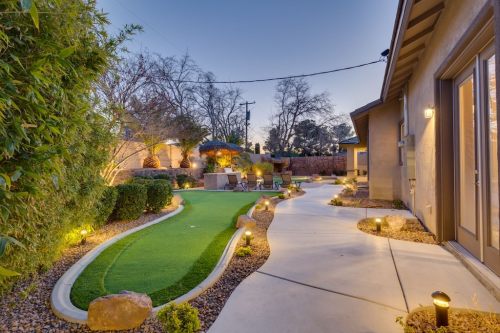A landscaped backyard with a putting green, pathway, and soft lighting, surrounded by trees and shrubs at dusk.