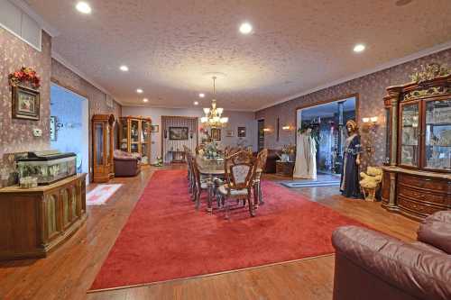 A spacious dining room with a large table, elegant chairs, a red carpet, and decorative furniture.