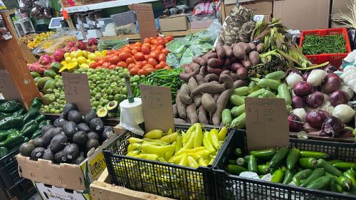 A vibrant market display featuring a variety of fresh vegetables and fruits, including peppers, tomatoes, and sweet potatoes.