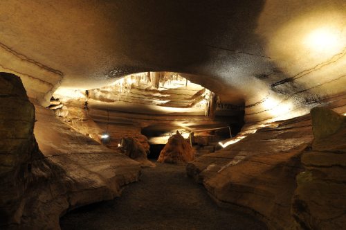 A dimly lit cave interior with layered rock formations and illuminated stalactites hanging from the ceiling.