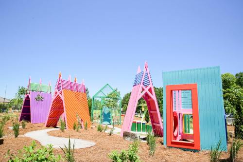 Colorful playground structures in vibrant hues of pink, orange, and teal, set against a clear blue sky.