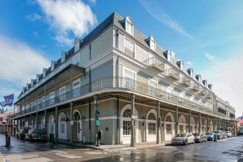 Historic building with a decorative balcony, located on a street with parked cars and a clear blue sky.