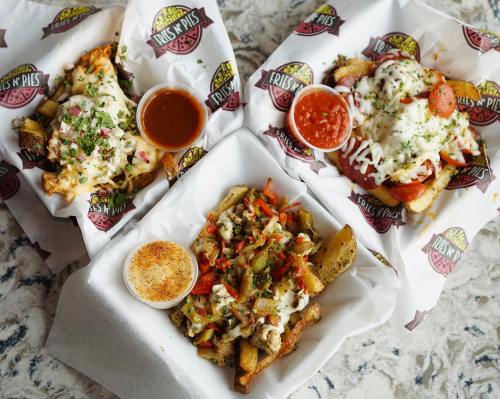 Three trays of loaded fries topped with cheese, meats, and sauces, garnished with herbs on a marble surface.