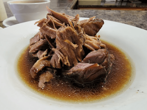 A plate of tender, shredded meat in a savory brown sauce, served on a white dish.