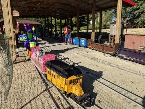 A miniature train on tracks in a covered area, with colorful decorations and people nearby.