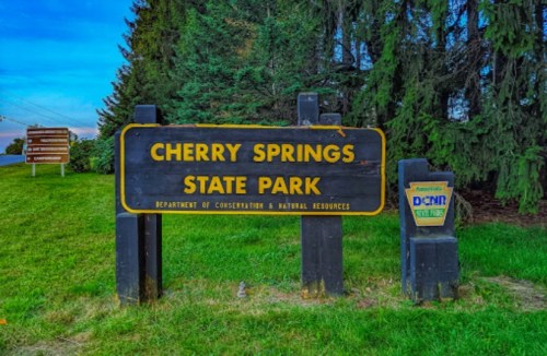 Sign for Cherry Springs State Park, surrounded by trees, with a blue sky in the background.