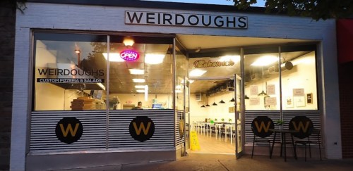 Exterior of Weirdoughs pizzeria with an open sign, featuring a modern design and outdoor seating.