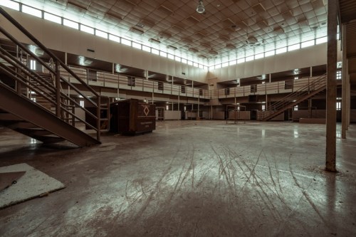 Abandoned interior of a large, empty building with metal staircases and large windows, casting natural light.
