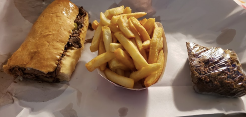 A sandwich with beef, a side of golden fries, and a wrapped dessert on a paper-lined tray.