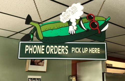 A cartoon pickle wearing sunglasses lounges above a sign that reads "PHONE ORDERS PICK UP HERE."