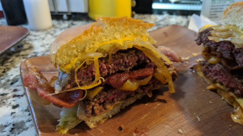 Close-up of a juicy burger with layers of bacon, cheese, and lettuce, served on a wooden plate.