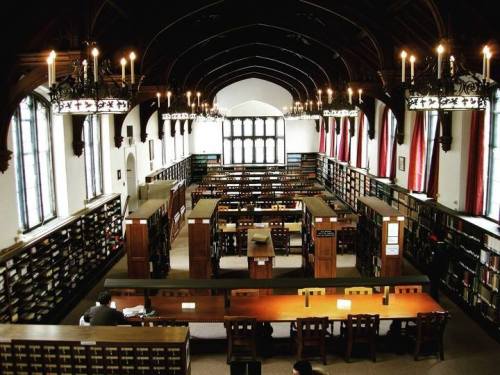 A spacious library with high ceilings, wooden shelves filled with books, and large windows letting in natural light.