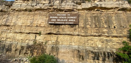 Sign on a rocky cliff reading "Welcome to Busiek State Forest and Wildlife Area, Missouri Conservation Department."