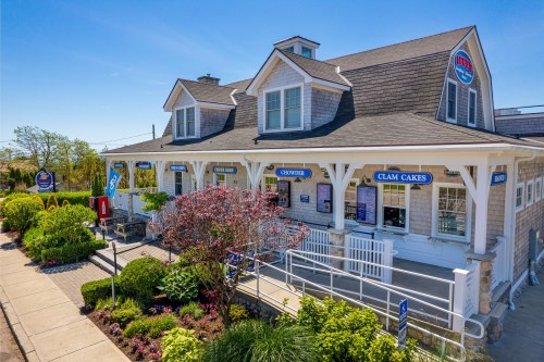 A charming seafood restaurant with a shingled exterior, colorful signage, and vibrant landscaping on a sunny day.