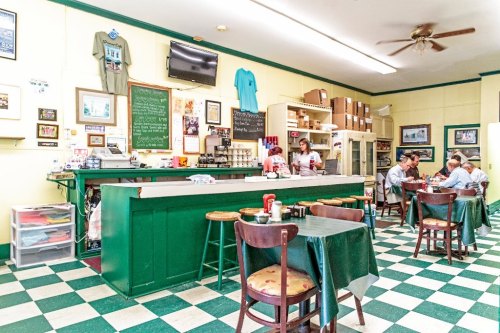 A cozy diner with green and white checkered floors, a counter, and patrons enjoying meals at tables.
